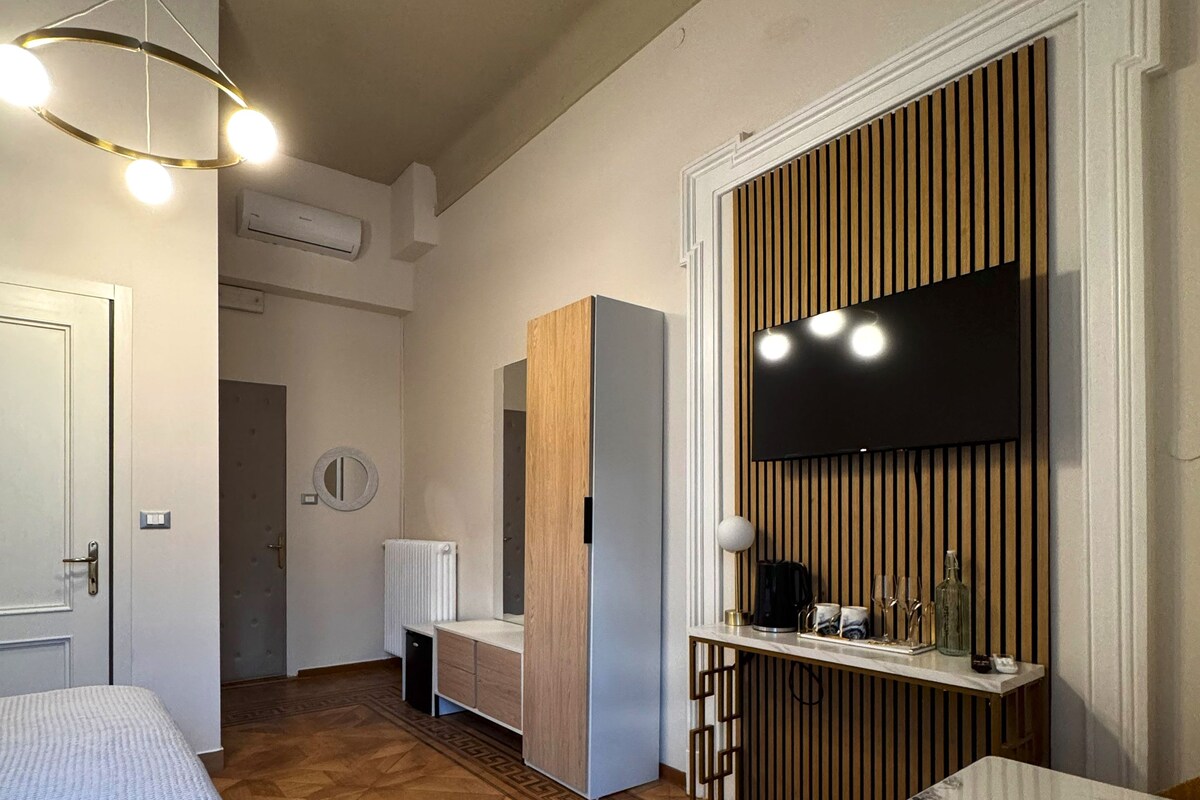 A modern hotel room with a bed, a small desk, a television, and a patterned floor.
