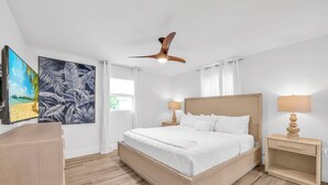 A hotel room with a bed, two bedside tables with lamps, a ceiling fan, and artwork on the walls. - Coastal Getaway w/ Pool, Spa & Tiki Lounge (Naples)