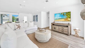 A modern living room with a white sofa, a round coffee table, and a large beach-themed painting on the wall. - Coastal Getaway w/ Pool, Spa & Tiki Lounge (Naples)