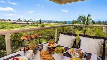 Desayuno con cruasanes, frutas y una jarra de jugo de naranja en un balcón con vistas panorámicas.
