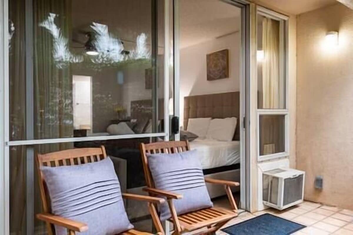 Una habitación con cama, ventana y dos sillas de madera con cojines.