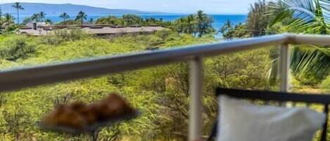 A balcony with a view of a coastal landscape, including palm trees and a distant mountain range.