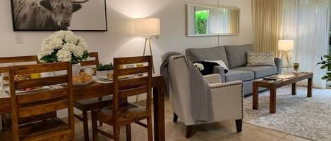A living room with a dining area, a grey sofa, a coffee table, and a lamp.