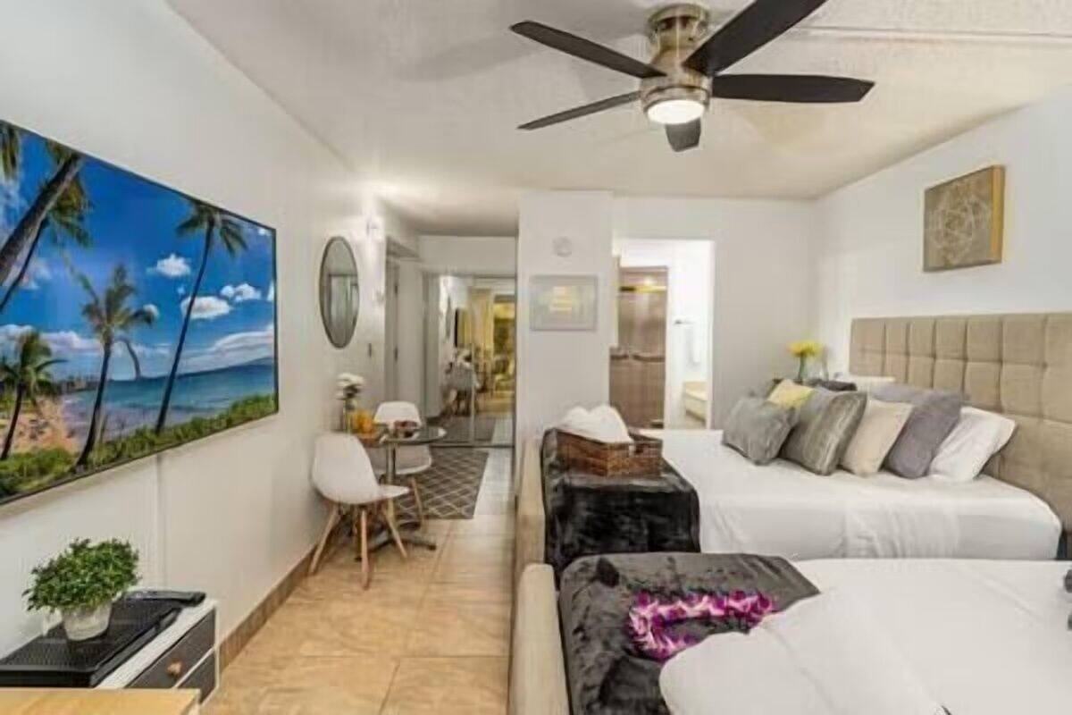 Une chambre d’hôtel moderne équipée d’un lit, d’un bureau, d’une chaise et d’un tableau représentant une scène de plage.