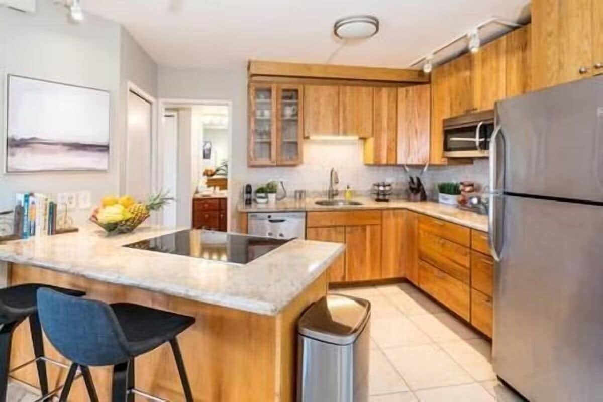 Una cocina moderna con armarios de madera, un refrigerador de acero inoxidable y una isla central con taburetes de bar.