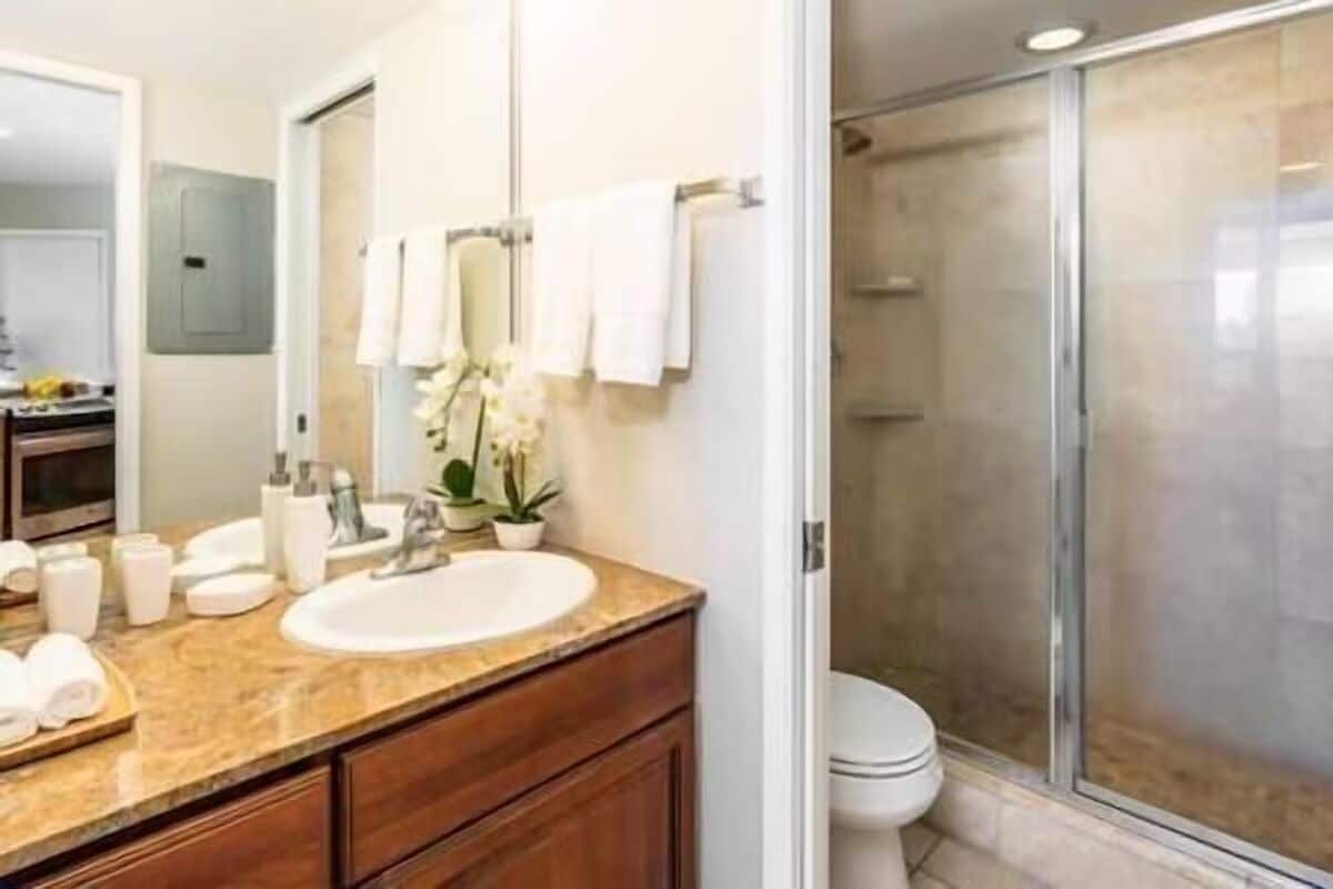 A bathroom with a marble sink, white towels, a mirror, and a glass shower enclosure.