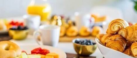 A breakfast setting with croissants, a plate of fruit, and a glass of orange juice.