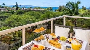 A breakfast table set on a balcony with a view of a tropical landscape.