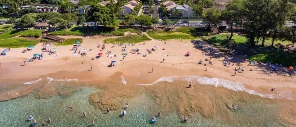Luchtbeeld van een strand met helder water, mensen die zwemmen en mensen die van het strand genieten.