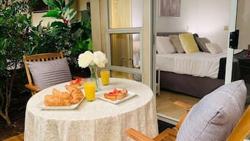 A dining area with a table set for breakfast, including croissants and juice, and a view of a bedroom with a bed and pillows.