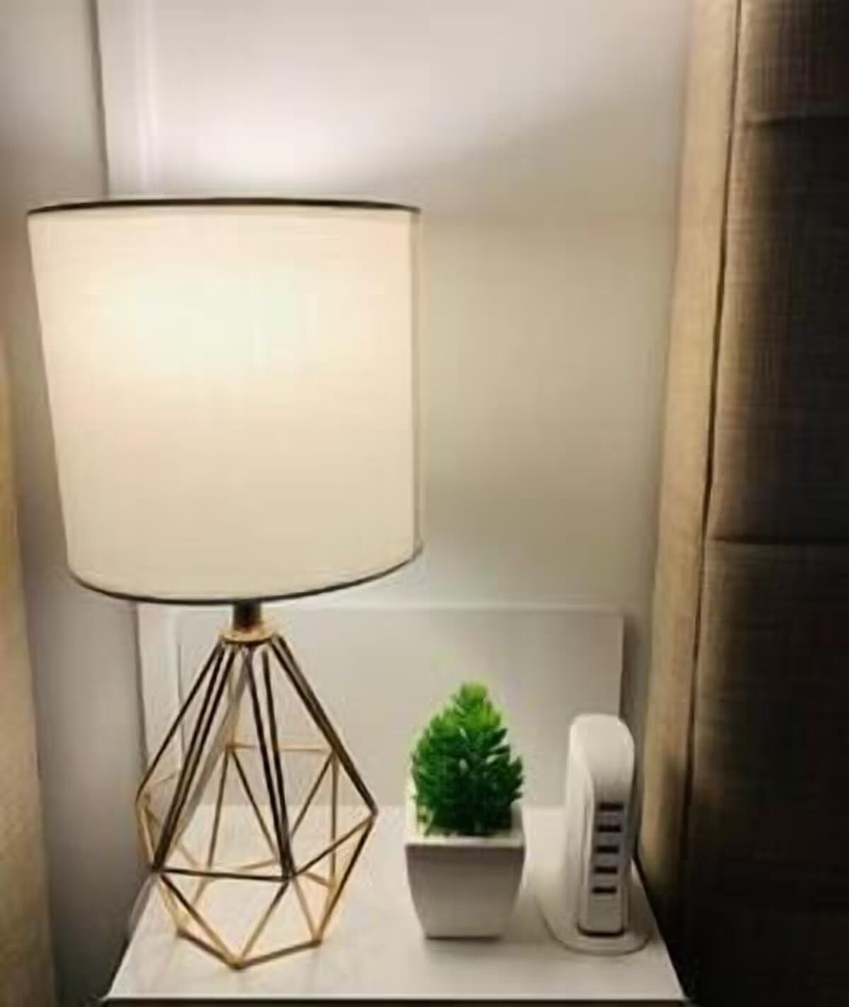 A bedside table with a lamp, a small potted plant, and a telephone.