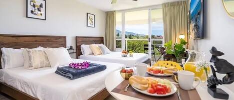 A hotel room with two beds, a dining table with breakfast, a ceiling fan, and a large window with a view.
