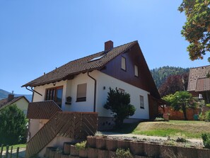A two-story house with a sloped roof, a wooden staircase, and a small garden area. - Apartment 'Am Rain' with Private Terrace, Garden, and Wi-Fi (Weisenbach)