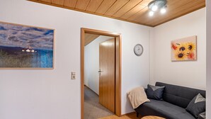 Una habitación con techo de madera, un sofá oscuro, una mesa de centro de madera, un cuadro de girasoles y un reloj en la pared.