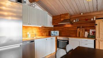 A modern kitchen with a stainless steel refrigerator, a microwave, and a built-in oven. There are wooden cabinets and a dark wooden dining table with chairs.