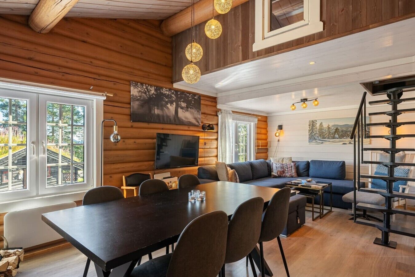 A log cabin interior with a dining area, seating, a TV, and a staircase.