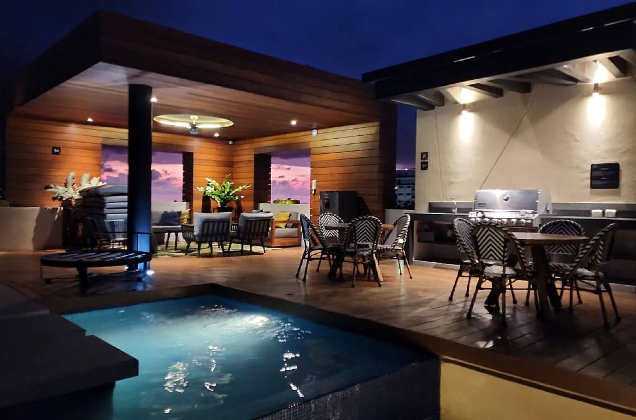 A modern outdoor patio with a pool, seating area, and barbecue setup.