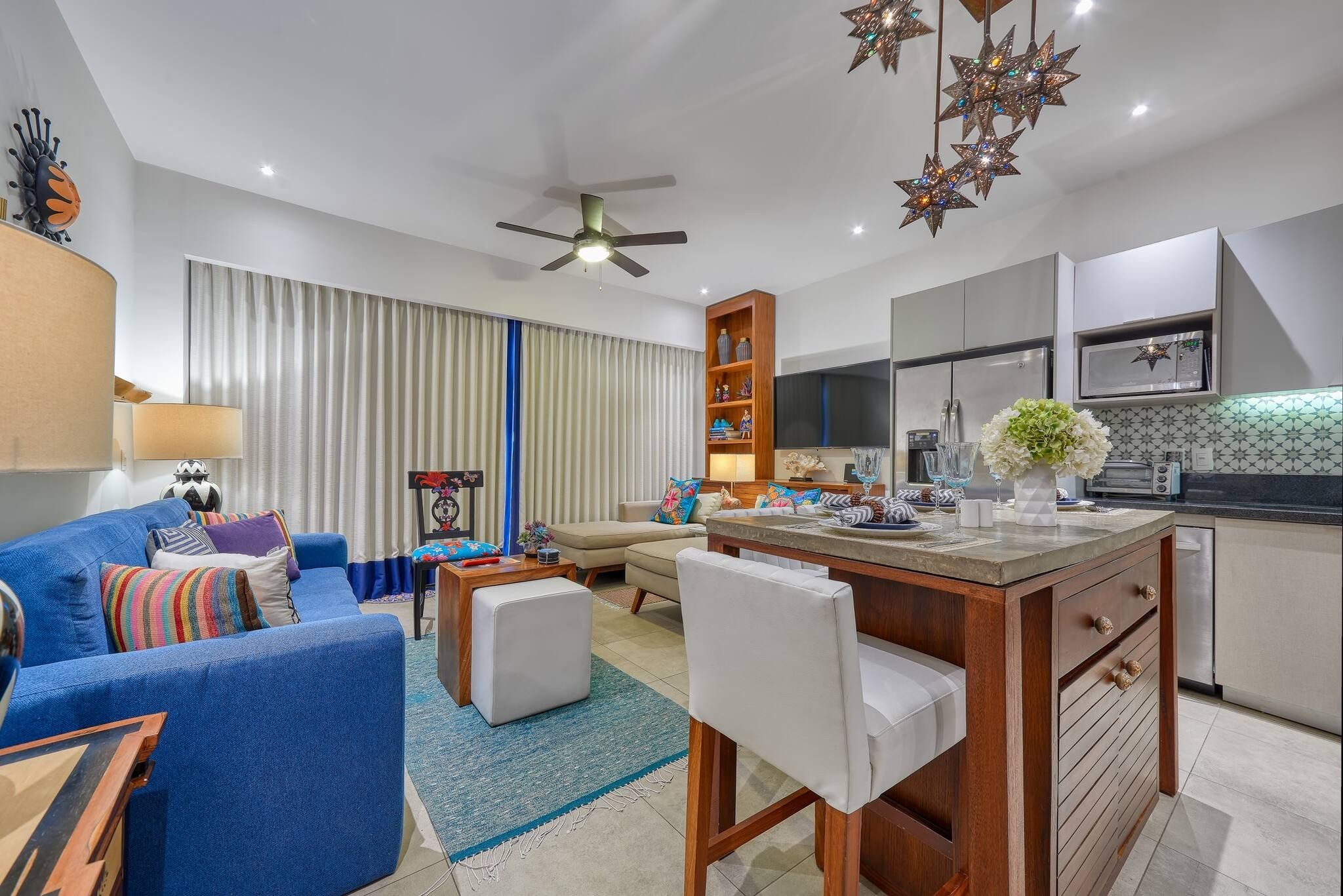 A modern living room with a blue sofa, a wooden coffee table, and a dining area with a kitchen in the background.
