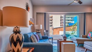 Una sala de estar moderna con sofá, reposapiés y una mesa de centro. Hay una lámpara en una mesita auxiliar y vistas al exterior a través de un ventanal grande.