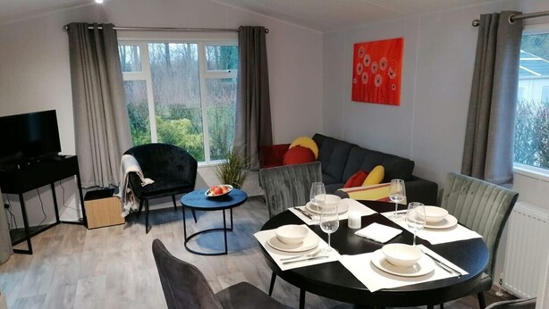 A modern living room with a dining area, a flat-screen TV, and a large window with curtains.