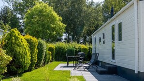 A mobile home with a patio, a grill, and a chair.