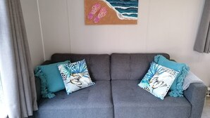 A grey sofa with two patterned cushions, a painting of a beach scene, and grey curtains. - Vakantiepark de Zeeuwse Parel - Summerlove (Scherpenisse)