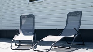 Two outdoor lounge chairs with metal frames and mesh backs, positioned on a tiled patio in front of a white house with horizontal siding. - Vakantiepark de Zeeuwse Parel - Summerlove (Scherpenisse)
