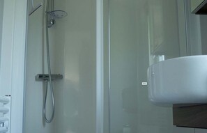 Eine Duschkabine aus Glas mit Handbrause und am Wand montierter Armatur.