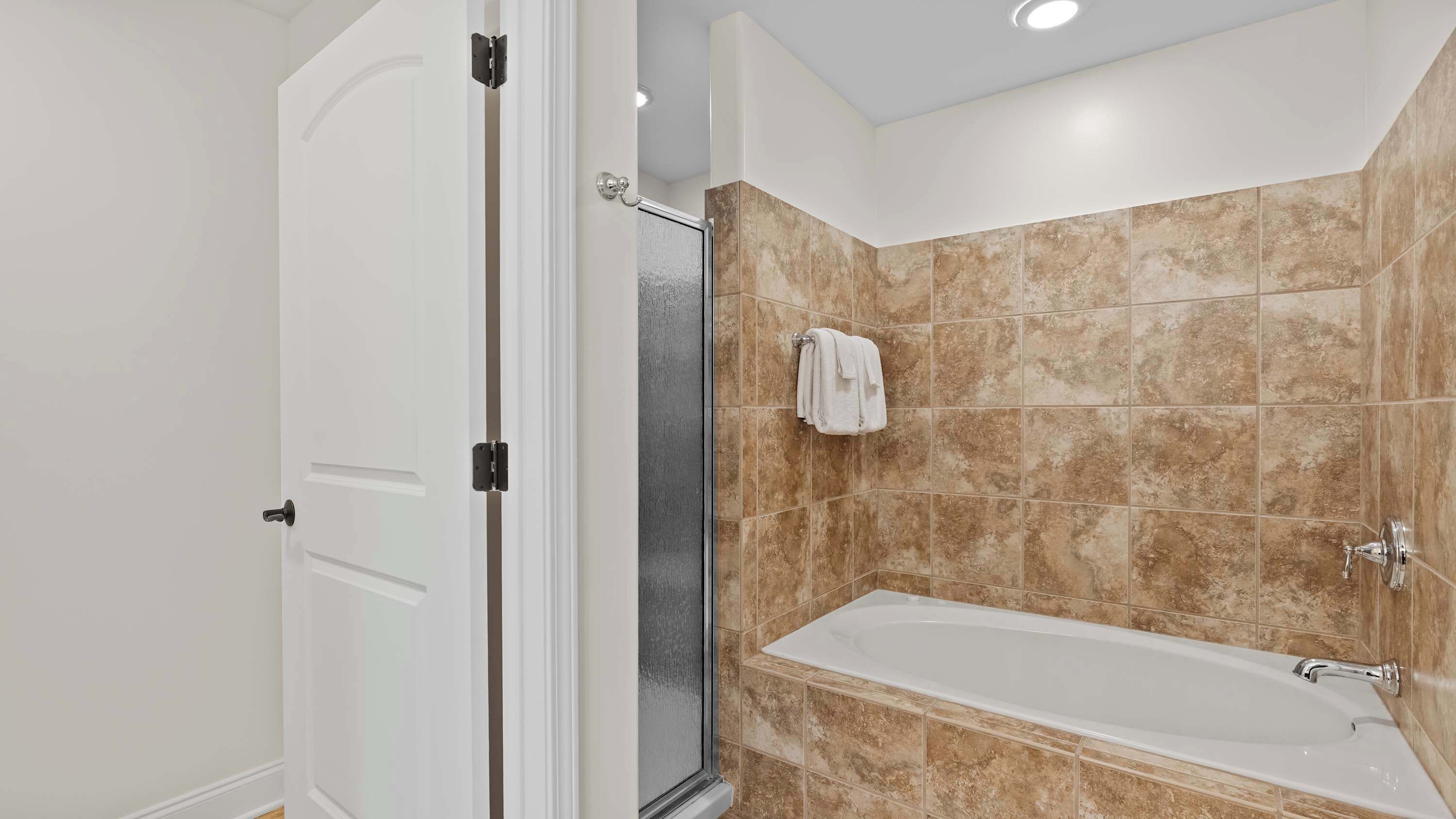 A modern bathroom with a walk-in shower, a bathtub, and beige tiled walls.