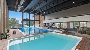 A modern indoor swimming pool with clear glass walls, a sun terrace, and a stone wall backdrop. - Avila Serenity Suites - For 6 (Lake Ozark)