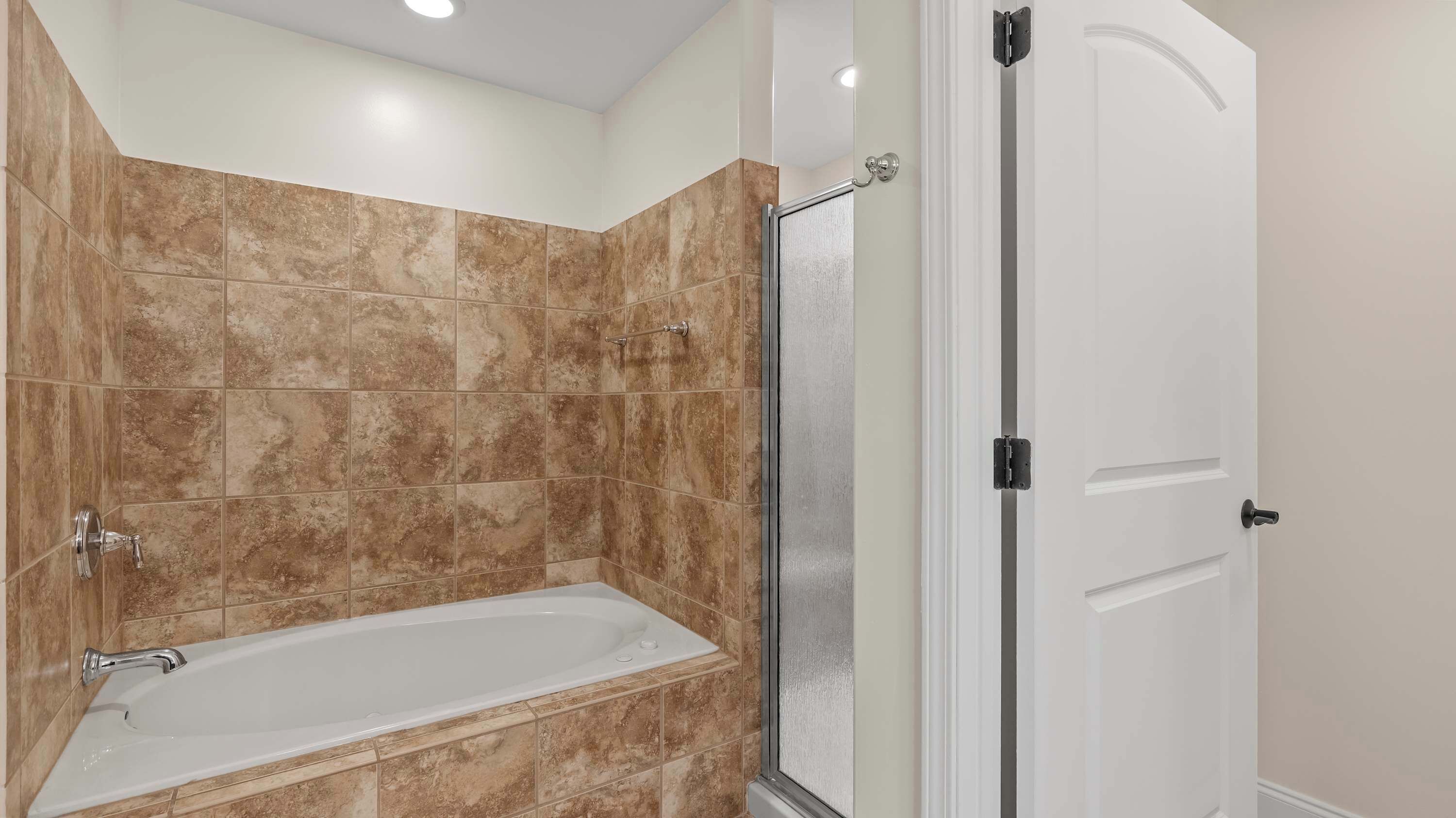 A bathroom with a bathtub, a shower, and a white door.