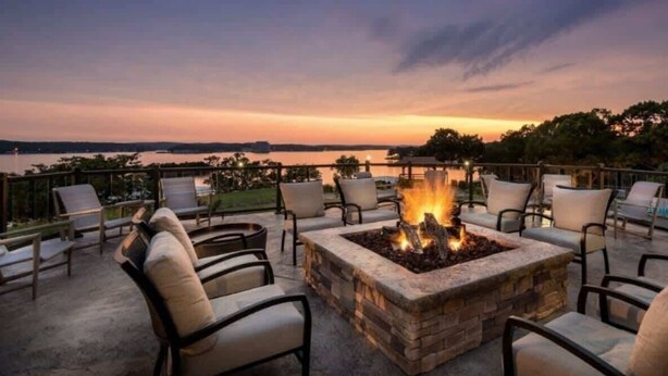 An outdoor seating area with a fire pit and chairs, overlooking a body of water during sunset. - Avila Serenity Suites - For 6 (Lake Ozark)