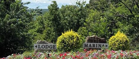 A signpost with directions to 'Lodge' and 'Marina' amidst a garden with colorful flowers and greenery.