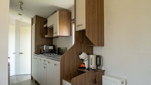 A compact kitchen with wooden cabinets, a stove, a kettle, and a microwave.
