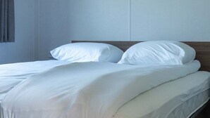 A neatly made bed with white linens and a wooden headboard in a room with plain walls.