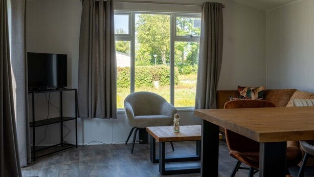 A room with a TV on a stand, a chair, a table, and a couch.