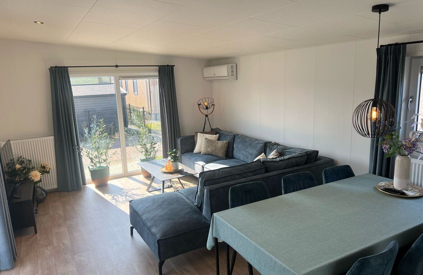 A modern living room with a sofa, a dining table, and a view through a sliding glass door to the outside.