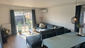 A modern living room with a sofa, a dining table, and a view through a sliding glass door to the outside.