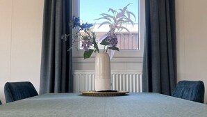A dining table with a vase of flowers, two chairs, and a window with curtains.