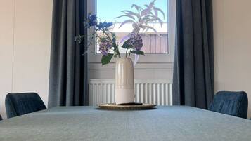 A dining table with a vase of flowers, two chairs, and a window with curtains.