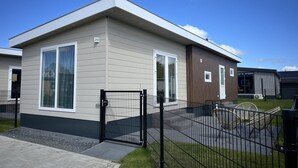 A modern single-story mobile home with a grey exterior, large windows, and a black metal gate.