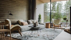 Ein modernes Wohnzimmer mit großem Fenster, einer Couch, zwei Sesseln, einem Couchtisch und einer Lampe.