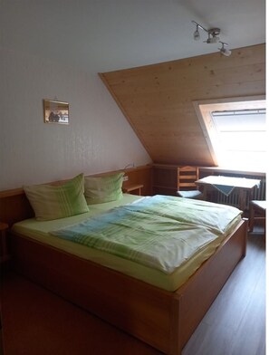 Une chambre avec un plafond en pente, un lit avec une literie verte, une petite table et une fenêtre.