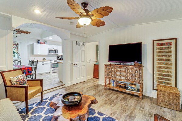 A living room with a television, a decorative cabinet, a dining area with a table and chairs, and a kitchen in the background.