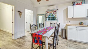 Un comedor con una mesa de madera, sillas y un ventilador de techo. Hay una zona de cocina con armarios y una encimera.