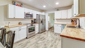 Cocina moderna con armarios blancos, electrodomésticos de acero inoxidable y encimera de madera.