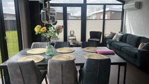 A modern dining area with a table set for six, surrounded by chairs, a vase with flowers, and a view of the outside.