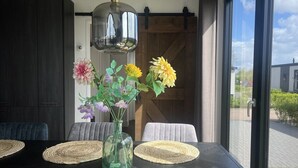 A dining table with a vase of flowers, a hanging light fixture, and a view of the outside.