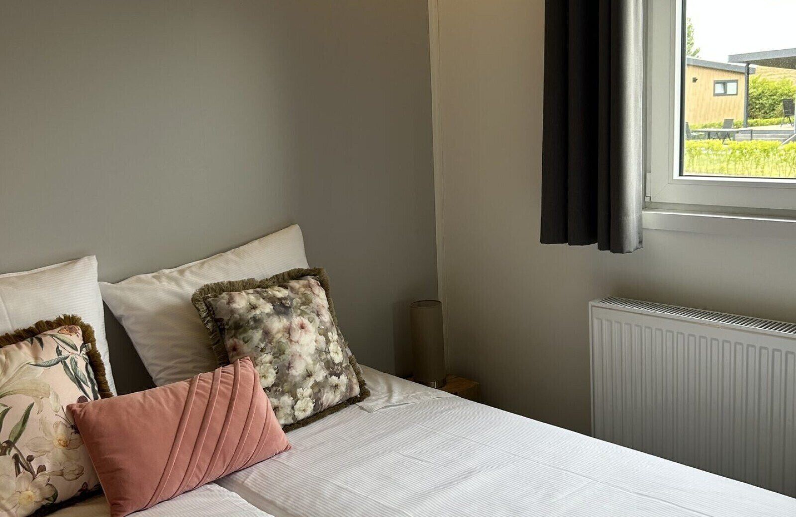 A bedroom with a bed, pillows, a window, and a radiator.