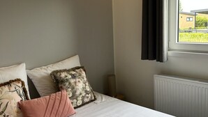 Een slaapkamer met een bed, kussens, een raam en een radiator.